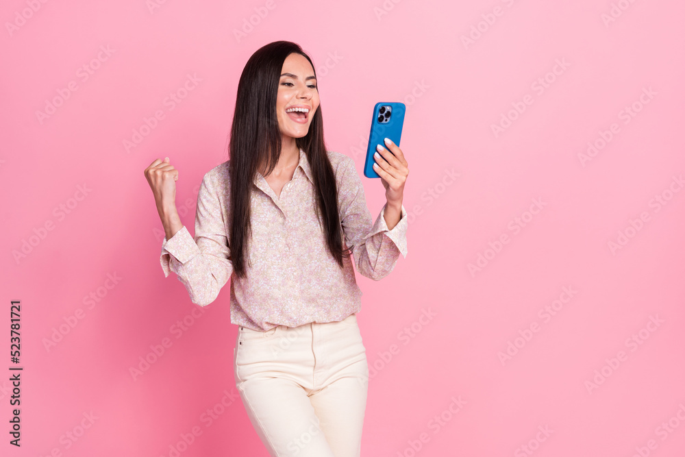 Photo portrait of excited young lady hold gadget raise fist job promotion wear stylish formalwear look isolated on pink color background Photo portrait of excited young lady hold gadget raise fist job promotion wear stylish formalwear look isolated on pink color background