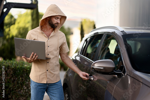 Bearded latin man trying to steal car using laptop and hacker software. Crime, carjacking concept photo