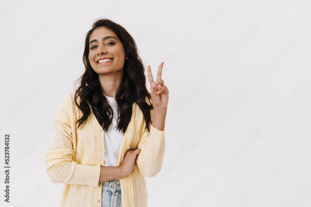 Young brunette indian woman smiling at camera and gesturing peace sign Young brunette indian woman smiling at camera and gesturing peace sign
