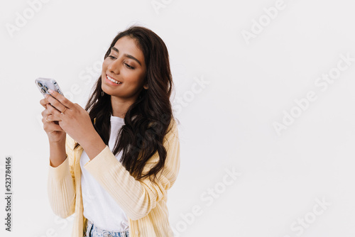 Young brunette indian woman smiling while using cellphone
