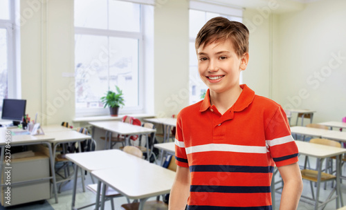 school, education and people concept - portrait of happy smiling student boy in red polo t-shirt over empty classroom background