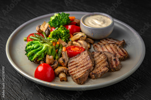 Hearty, dietary dish. Salad with beef, vegetables and tuna sauce in a ceramic plate on a dark textured background. Restaurant menu Isolated on black