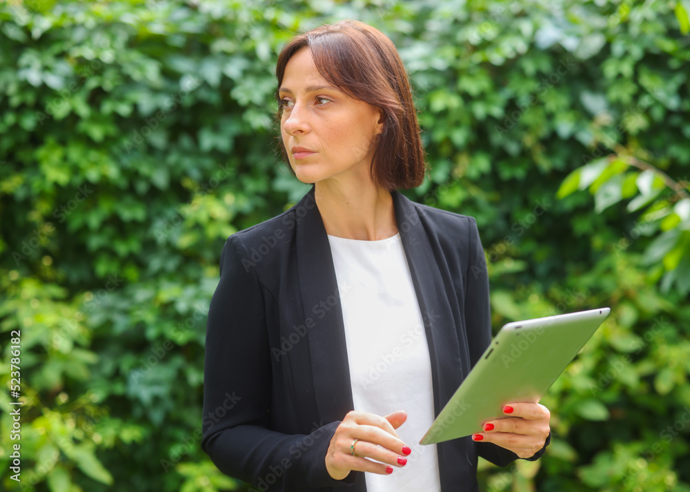 business woman uses a tablet against the background of green plants. portrait of a business woman with a tablet business woman uses a tablet against the background of green plants. portrait of a business woman with a tablet