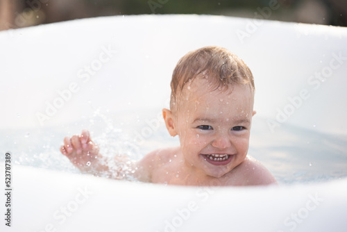 A small child swims in an inflatable pool. A child swims and splashes in the pool. Summer vacation for children. © Anastasia