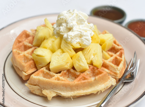 Belgium waffles with sliced pineapple and ice cream on a plate with chocolate toping and fruit sauce