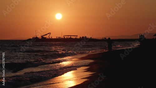 People walk along the seashore during sunset, 4K video, shot in backlight