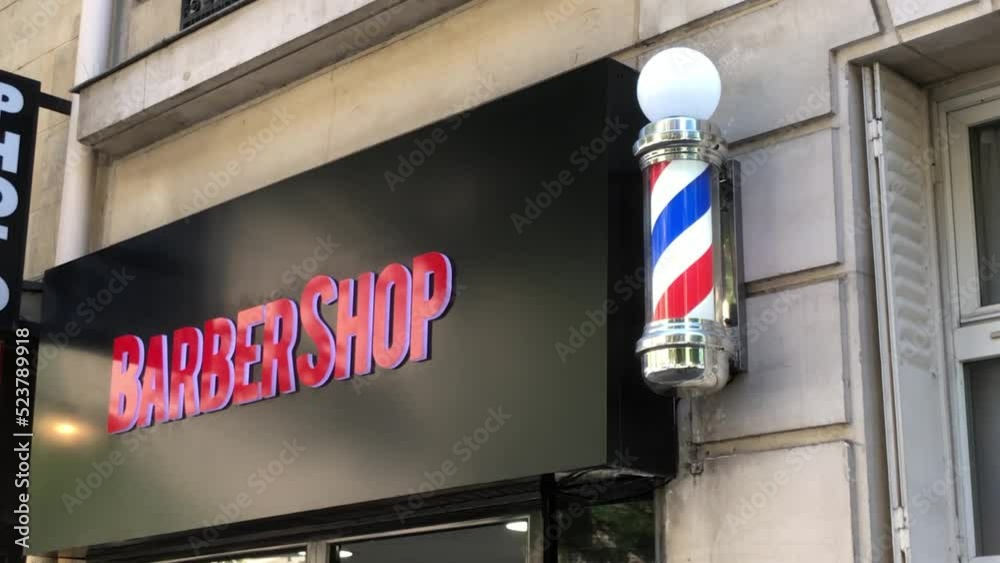 vidéo d'une enseigne noire avec comme inscription Barbershop en rose et à coté accroché au mur le poteau du barbier de couleur blanc rouge et bleu