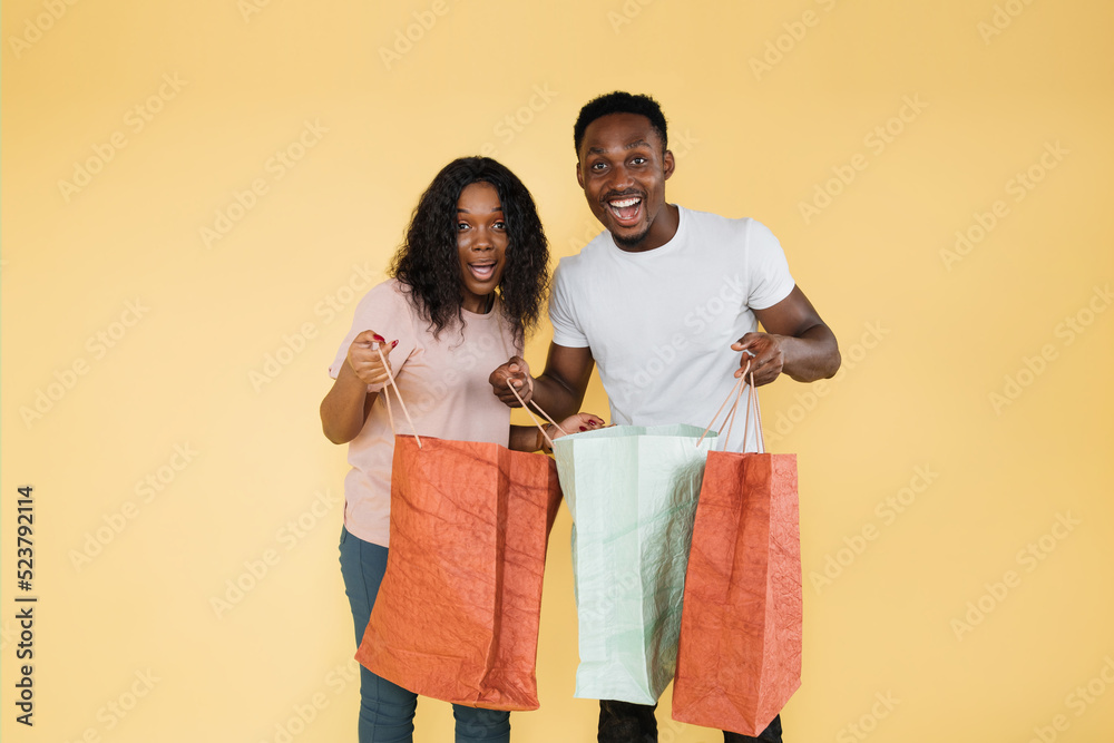 Excited african american woman and man look at camera other and hold shopping bags. Happy curly girl and guy in casual clothes happy that making purchases. Excited african american woman and man look at camera other and hold shopping bags. Happy curly girl and guy in casual clothes happy that making purchases.