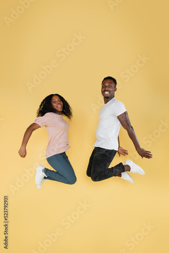 Full length shot of jumping african couple having fun together. Studio photo of young people on yellow background, copy space