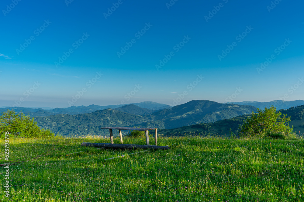 Carpathians mountains landscapes from green meadow with bench on sunrise, Apetska mountain.
