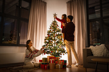family, winter holidays and people concept - happy mother, father and little daughter decorating christmas tree at home