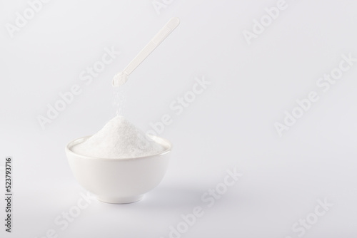 A small spoon pours the sugar substitute into the bowl. Vertical photo of a sugar substitute on a white background in a white bowl. Stevia.