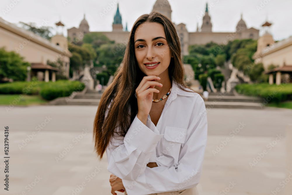 Close up outside portrait of elegant pretty woman with loose dark hair, tanned skin and wonderful smile posing at camera outdoor on city background in summer evening Close up outside portrait of elegant pretty woman with loose dark hair, tanned skin and wonderful smile posing at camera outdoor on city background in summer evening