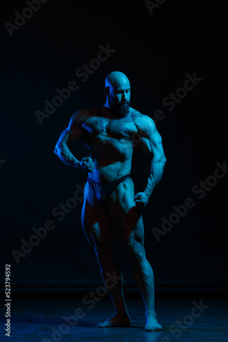 Athletic man demonstrates muscles in the light of a blue light filter on a dark background. © ksi