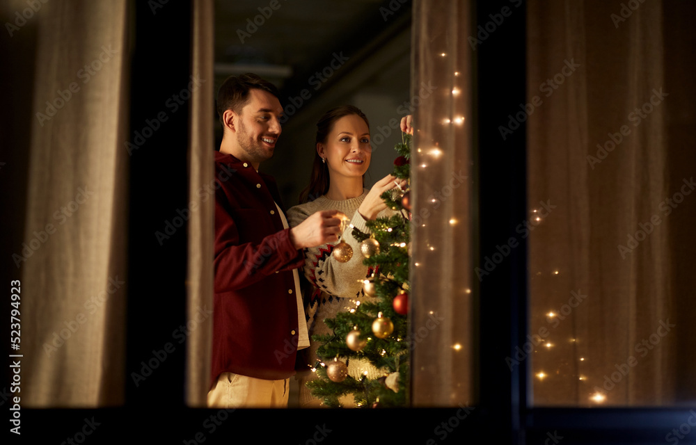 winter holidays and people concept - happy couple decorating christmas tree at home