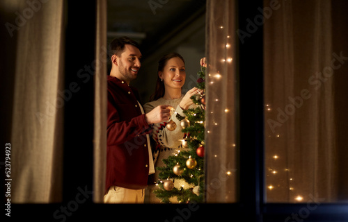 winter holidays and people concept - happy couple decorating christmas tree at home