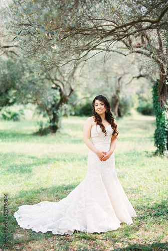 Bride in a white mermaid dress stands near a tree in an olive grove