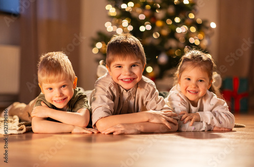 christmas, winter holidays and childhood concept - happy little girl and boys lying on floor at home