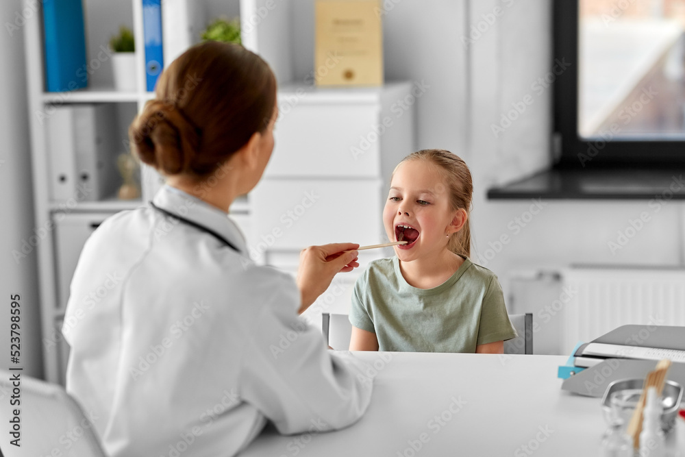 Obraz premium medicine, healthcare and pediatry concept - female doctor or pediatrician with tongue depressor checking little girl patient's throat on medical exam at clinic