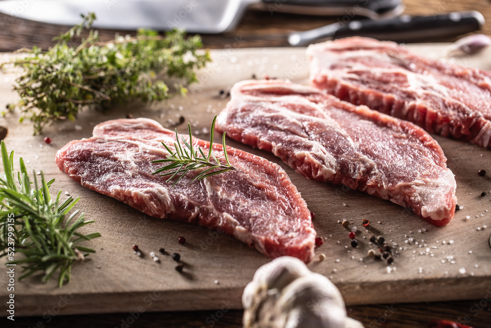 Raw pork neck cut on a cutting board with rosemary and thyme herbs Raw pork neck cut on a cutting board with rosemary and thyme herbs
