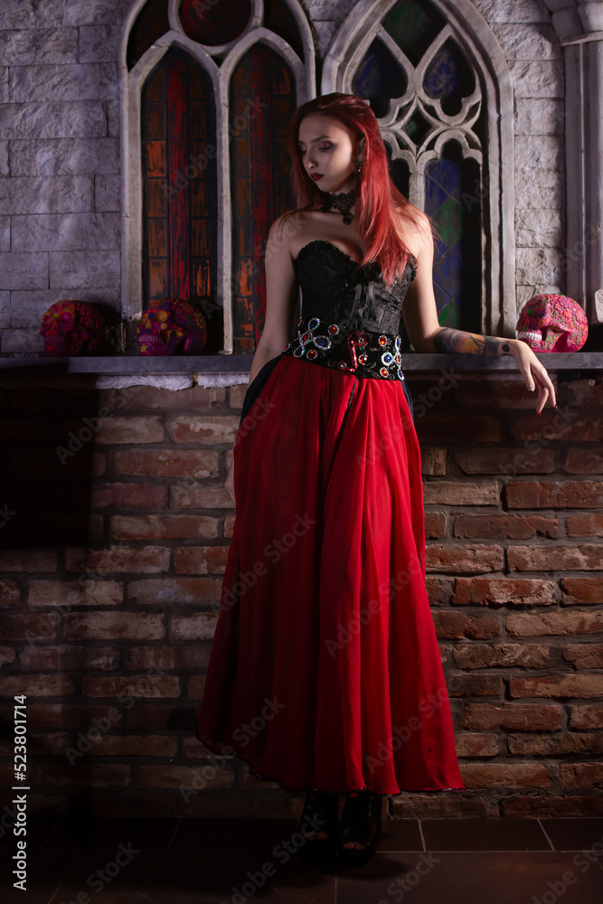 Beautiful young sexy woman vampire in medieval dark castle. Red gothic evening dress with corset.
