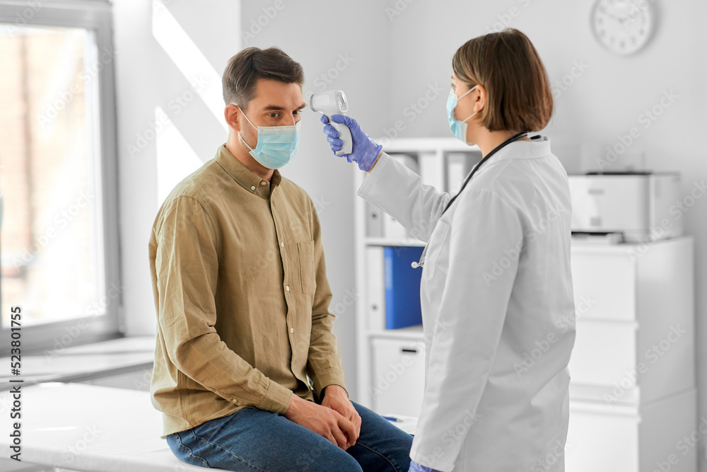Obraz premium medicine, healthcare and people concept - female doctor in mask with infrared forehead thermometer measuring temperature of man patient at hospital