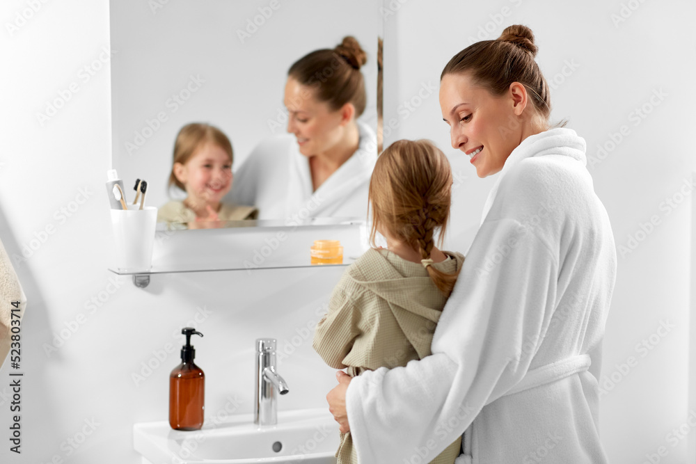 beauty, hygiene and people concept - happy smiling mother and daughter looking to mirror in bathroom beauty, hygiene and people concept - happy smiling mother and daughter looking to mirror in bathroom