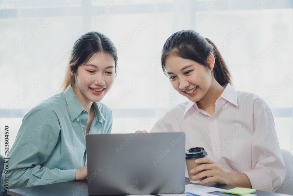 Two young Asian businesswoman discuss investment project working and planning strategy. Business people talking together with laptop computer at office. Two young Asian businesswoman discuss investment project working and planning strategy. Business people talking together with laptop computer at office.