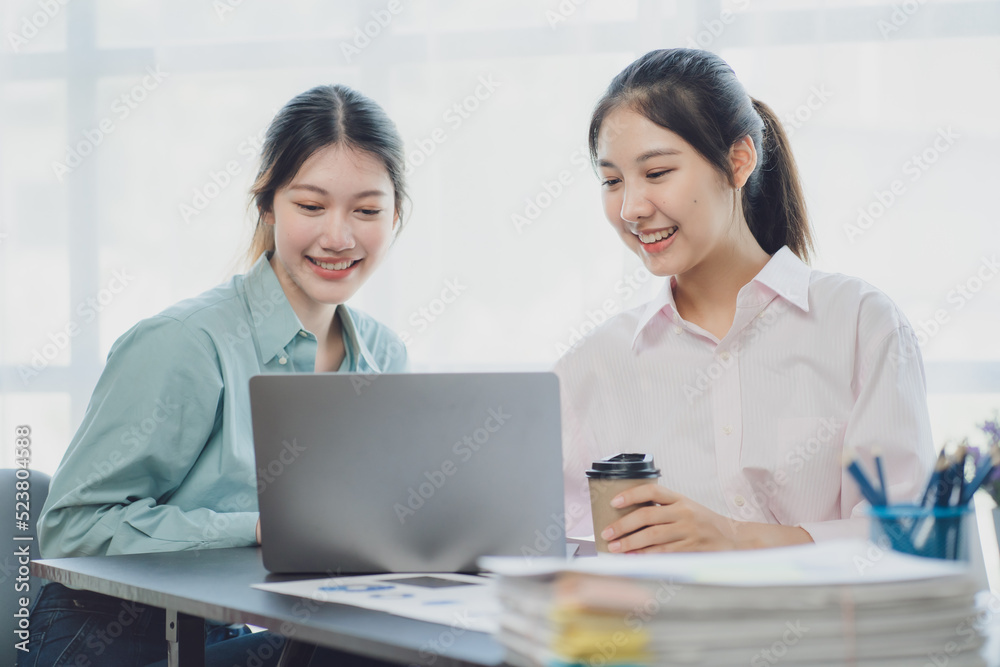 Two young Asian businesswoman discuss investment project working and planning strategy. Business people talking together with laptop computer at office. Two young Asian businesswoman discuss investment project working and planning strategy. Business people talking together with laptop computer at office.
