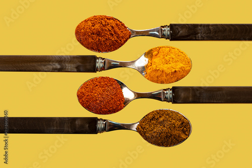 A selection of cayenne pepper tumeric chilli curry powder spices used in Indian cooking on a coulerful yellow background photo