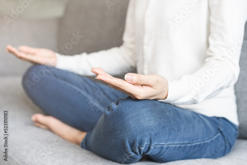 Beautiful asian young woman, girl hands in calm pose sitting practice meditating in lotus position on sofa at home, meditation, exercise for wellbeing, healthy care. Relaxation, happy leisure people.
