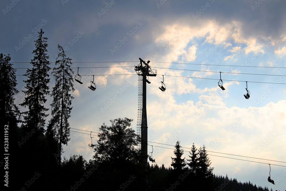 Silhouette of a chairlift over a forest on a mountain slope