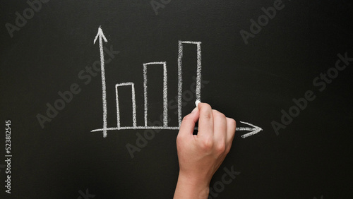 A hand draws a growing graph with chalk on a blackboard