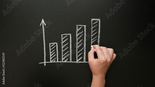 A hand draws a growing graph with chalk on a blackboard