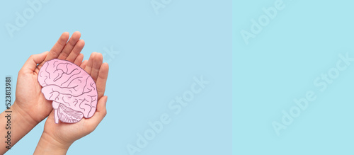 Woman hands holding human brain shape made from paper on light blue background. Awareness of Alzheimer, Parkinson's disease, dementia, stroke, seizure or mental health. Neurology and Psychology care.