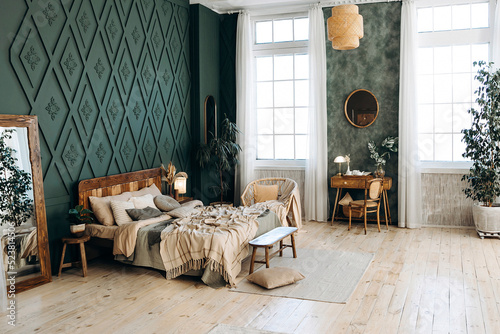 Bild auf Leinwand Cozy bedroom interior in boho style with wooden furniture, console table, textiles, green walls, large windows and potted plants