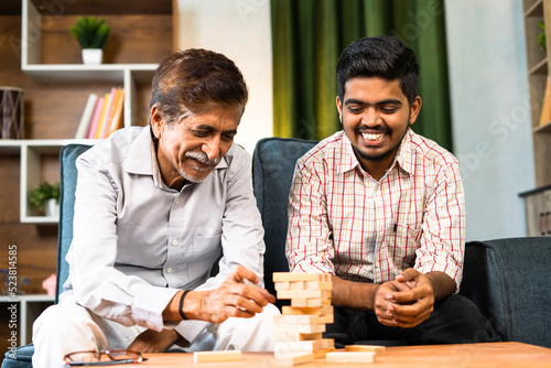 Fotografie Excited grandfather with grandson playing tumbling tower game while sitting at home - concept of leisure activity, entertainment and family bonding