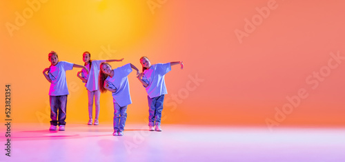 Dance group of happy  active little girls in t-shirts and jeans in action isolated on orange background in neon. Concept of music  fashion  art  childhood