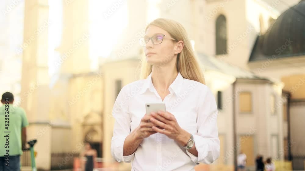Attractive middle aged businesswoman in the city street with phone. Lady in eyeglasses hold smartphone, watching social media in the centre. Attractive middle aged businesswoman in the city street with phone. Lady in eyeglasses hold smartphone, watching social media in the centre.