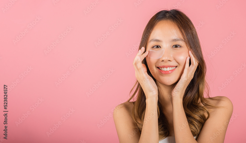 Anti aging. Asian beautiful young woman smiling mask cosmetic patches gel under the eyes, Portrait female applying medical hydrogel eye patch on face, studio shot isolated on pink background, skincare Anti aging. Asian beautiful young woman smiling mask cosmetic patches gel under the eyes, Portrait female applying medical hydrogel eye patch on face, studio shot isolated on pink background, skincare