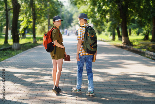 portrait of students in a city park, teenage schoolchildren a boy and a girl walking along a path, rear view