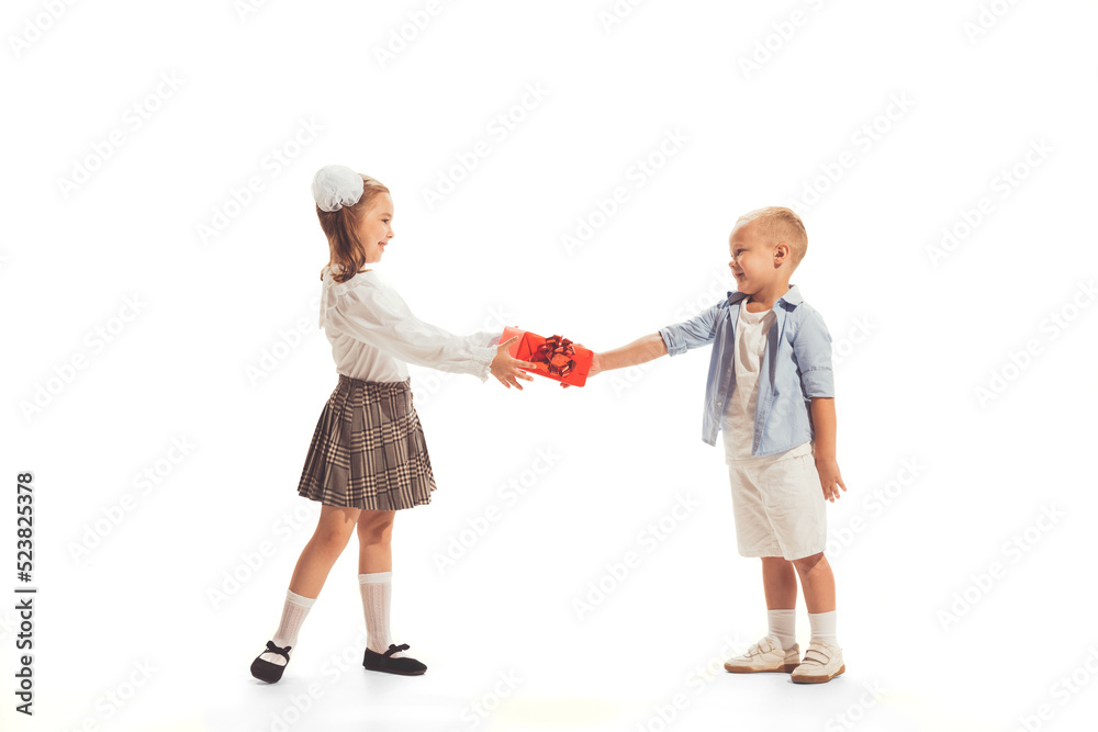 Portrait of beautiful little children, boy giving present box to girl isolated over white studio background.