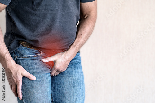 A man holds his crotch with his hand. The place of pain is marked in red. Urinary incontinence, enuresis. Inflammation of the bladder. The concept of medicine. photo