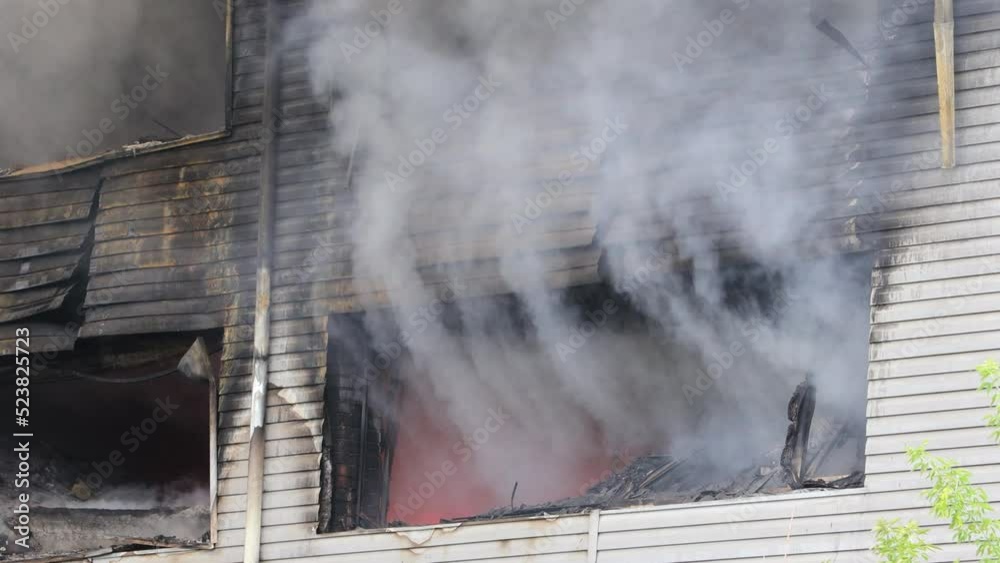 Puffs of heavy gray smoke and bright orange flames from broken windows during a major industrial building fire