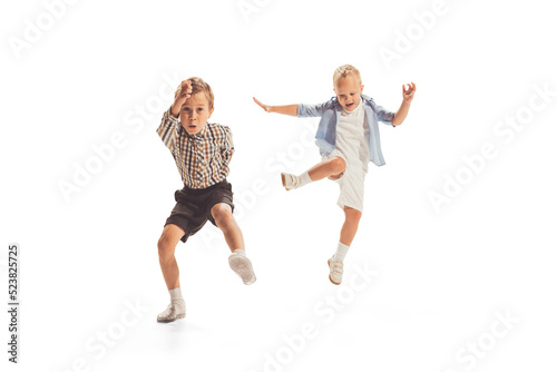 Portrait of two little boys, children playing together, running, jumping isolated over white studio background