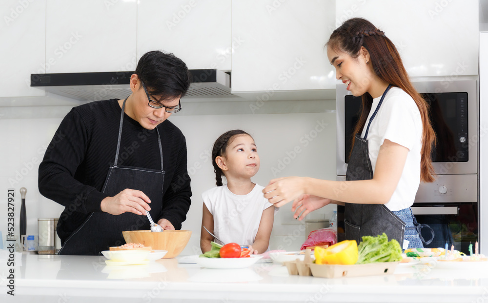 A happy family cooks together in the kitchen. Father, mother, and cute little daughters prepare dishes for salads A happy family cooks together in the kitchen. Father, mother, and cute little daughters prepare dishes for salads