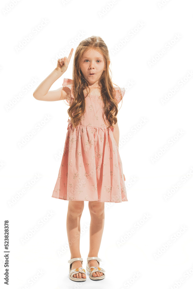 Portrait of beautiful little girl in stylish dress posing, raising finger up isolated over white studio background