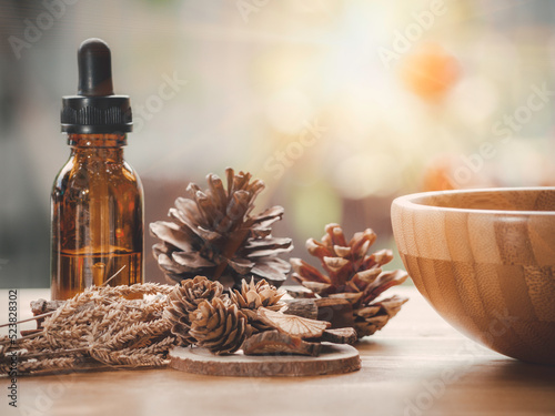 Dark glass bottle with essential oil blend with cinnamon, dried citrus slice, pine twigs, cones and wooden background. Nature home deodorants and warm toned.