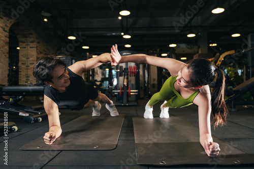 Young Asian male and female planking exercise in fitness gym for building a beautiful slim body. Professional trainer coach helping young woman exercising in the sport gym.