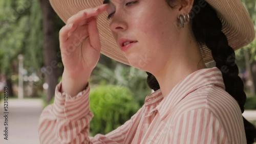 Sunstroke and heatstroke. Closeup of sweaty woman in a straw hat is standing on the street, fanning herself with her hand from the heat. Summer vacation and hot temperature.
